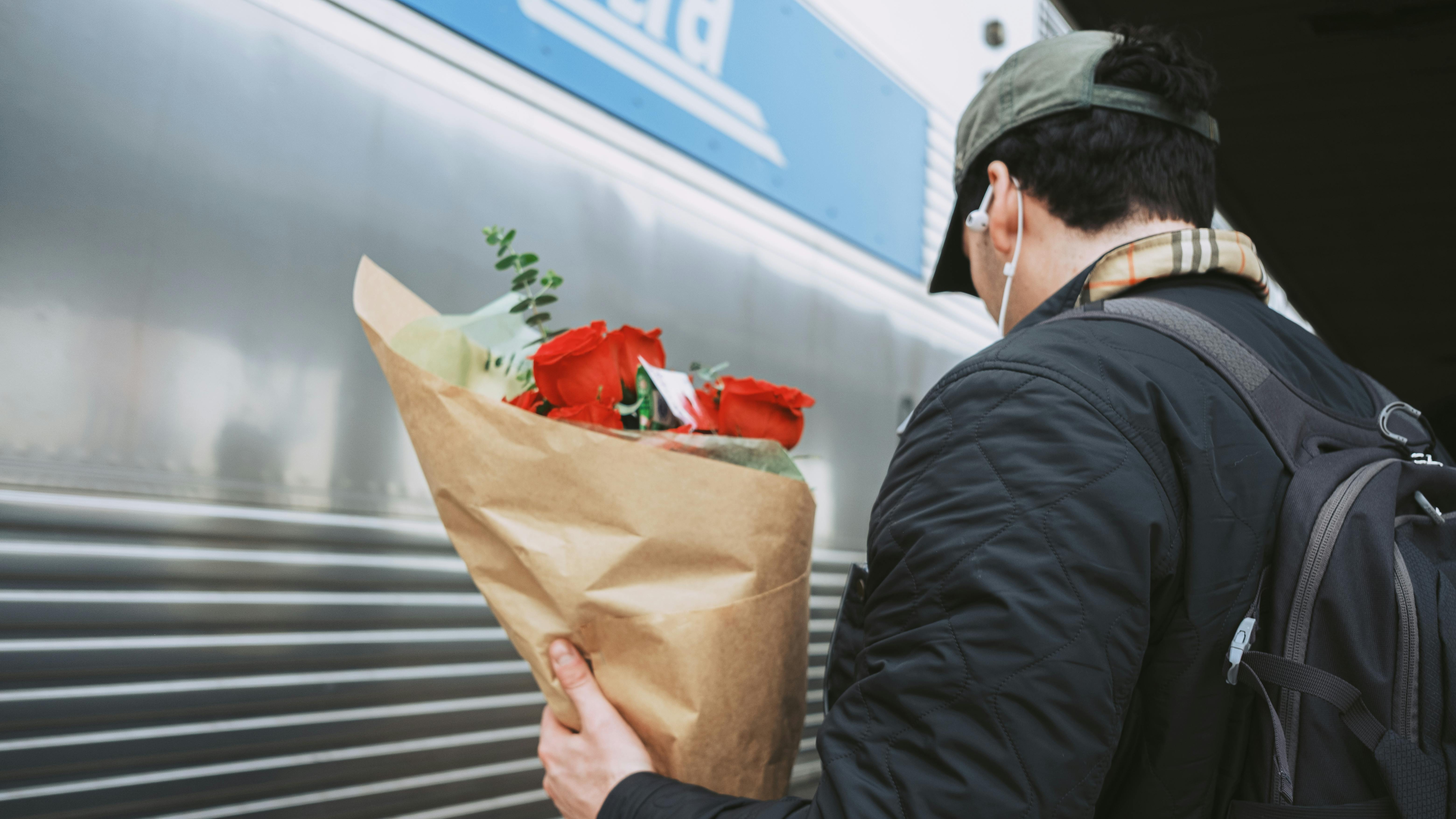 Δωρεάν Ένας άντρας που κρατά κόκκινα τριαντάφυλλα κοντά σε ένα τρένο, υποδηλώνοντας ταξίδι ή μια ρομαντική χειρονομία. Φωτογραφία από στοκ φωτογραφιών