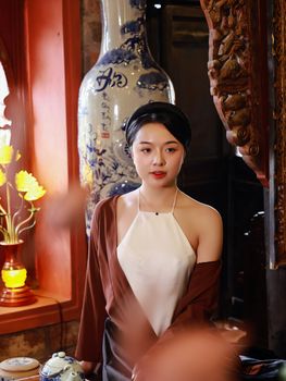 Woman posing gracefully indoors with cultural decor and soft lighting.