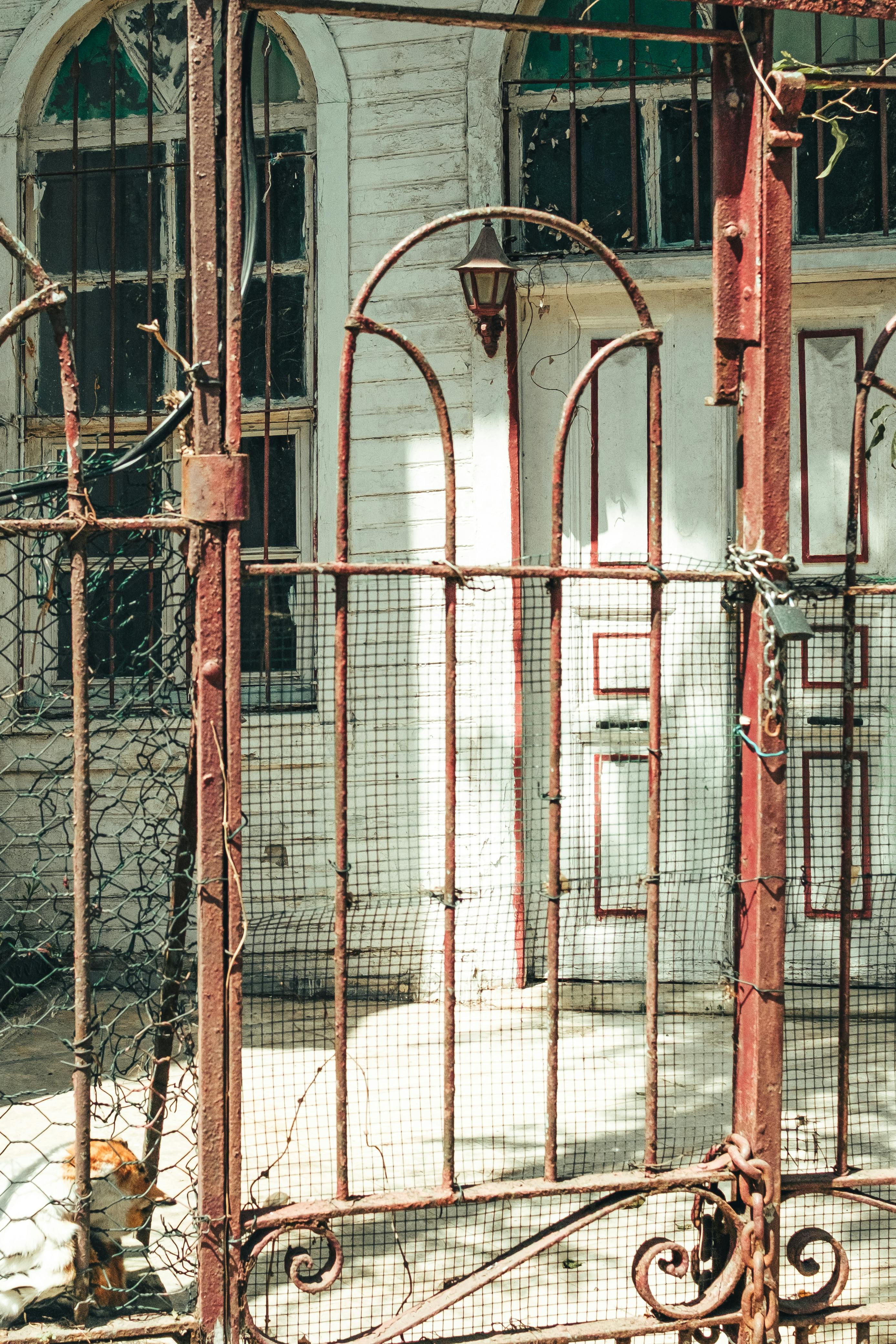 Gratis Una puerta de hierro oxidada que conduce a una casa antigua y transmite una atmósfera vintage. Foto de stock