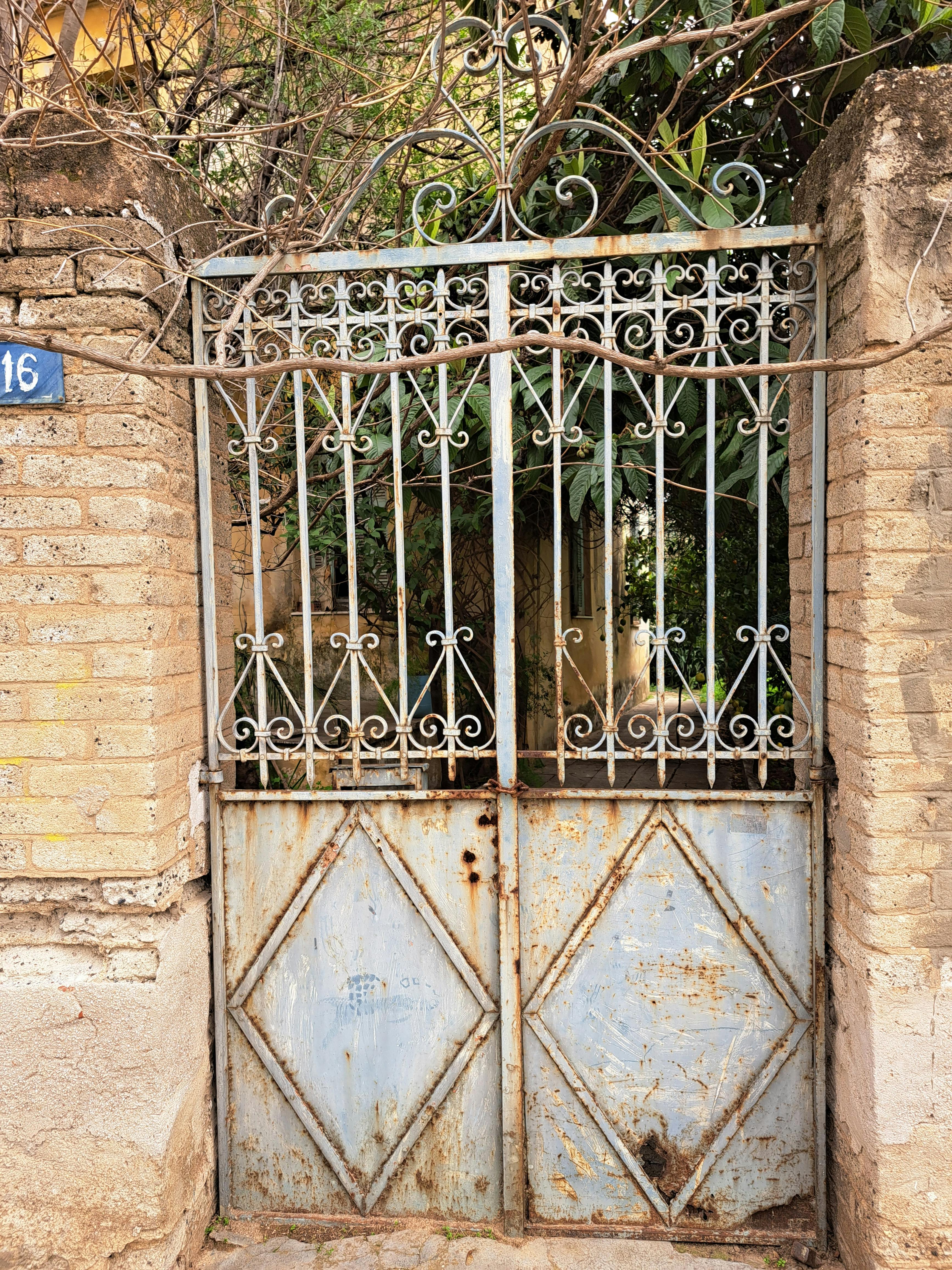 Gratis Cancello rustico in ferro con dettagli decorati, circondato da muri in mattoni, che aggiungono un fascino vintage. Foto a disposizione