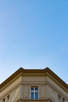 Elegant classical building corner against a clear blue sky, featuring detailed architectural elements.
