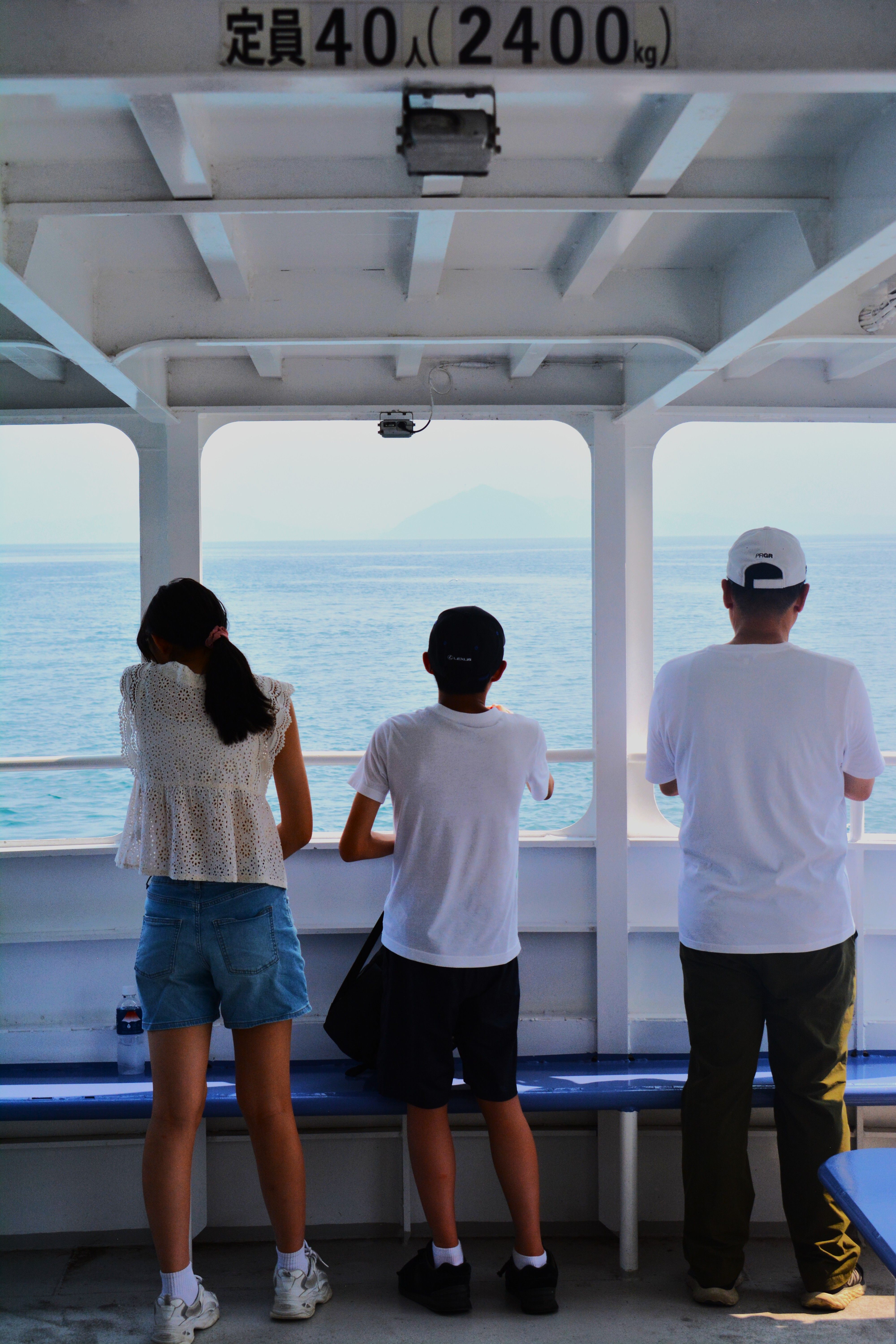 Three individuals relaxing on a ferry, gazing at the sea, enjoying a serene ocean view.