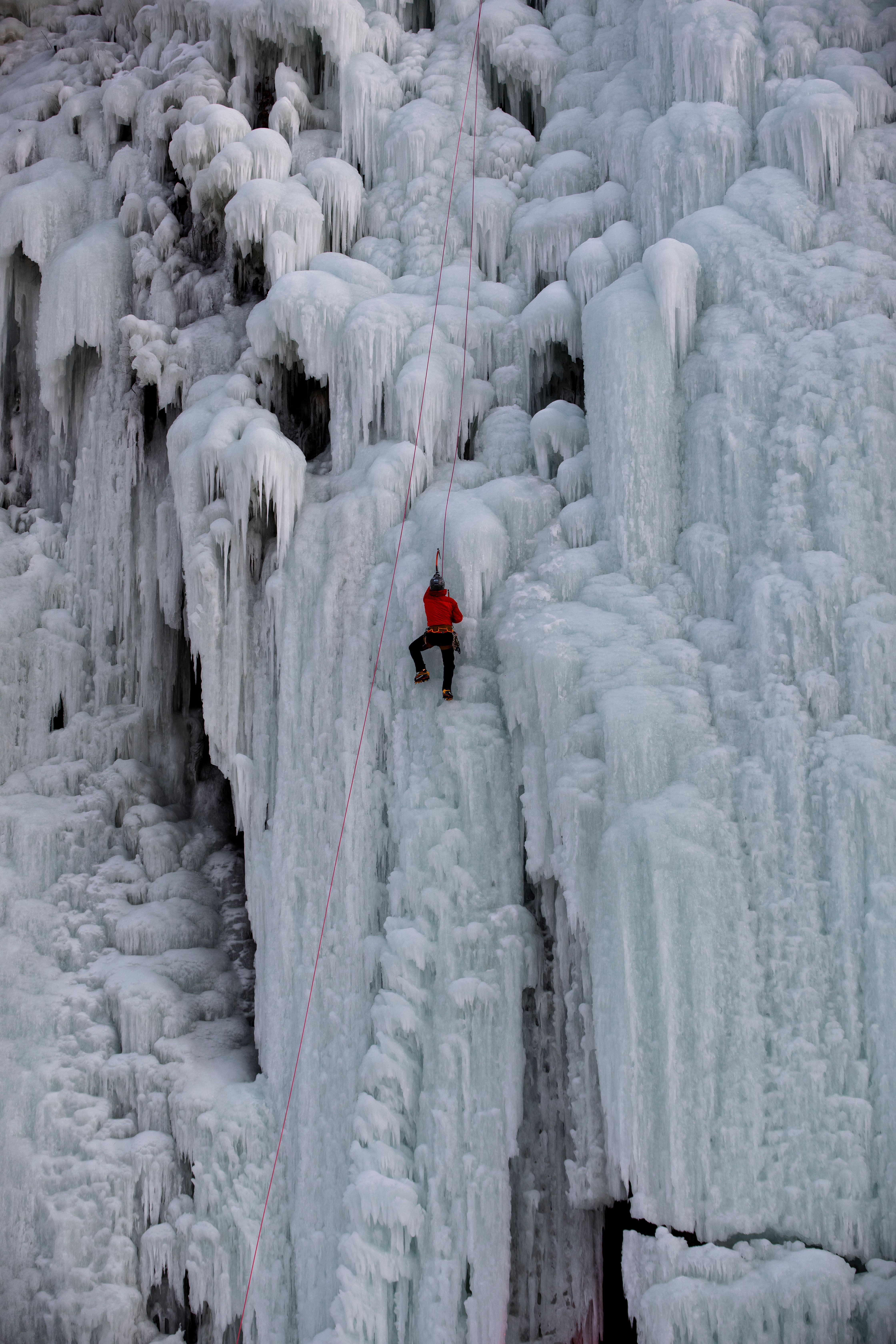 A daring ice climber scales a massive frozen waterfall in winter, showcasing adventure.