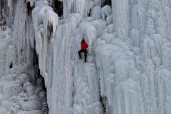 A daring ice climber scales a massive frozen waterfall in winter, showcasing adventure.