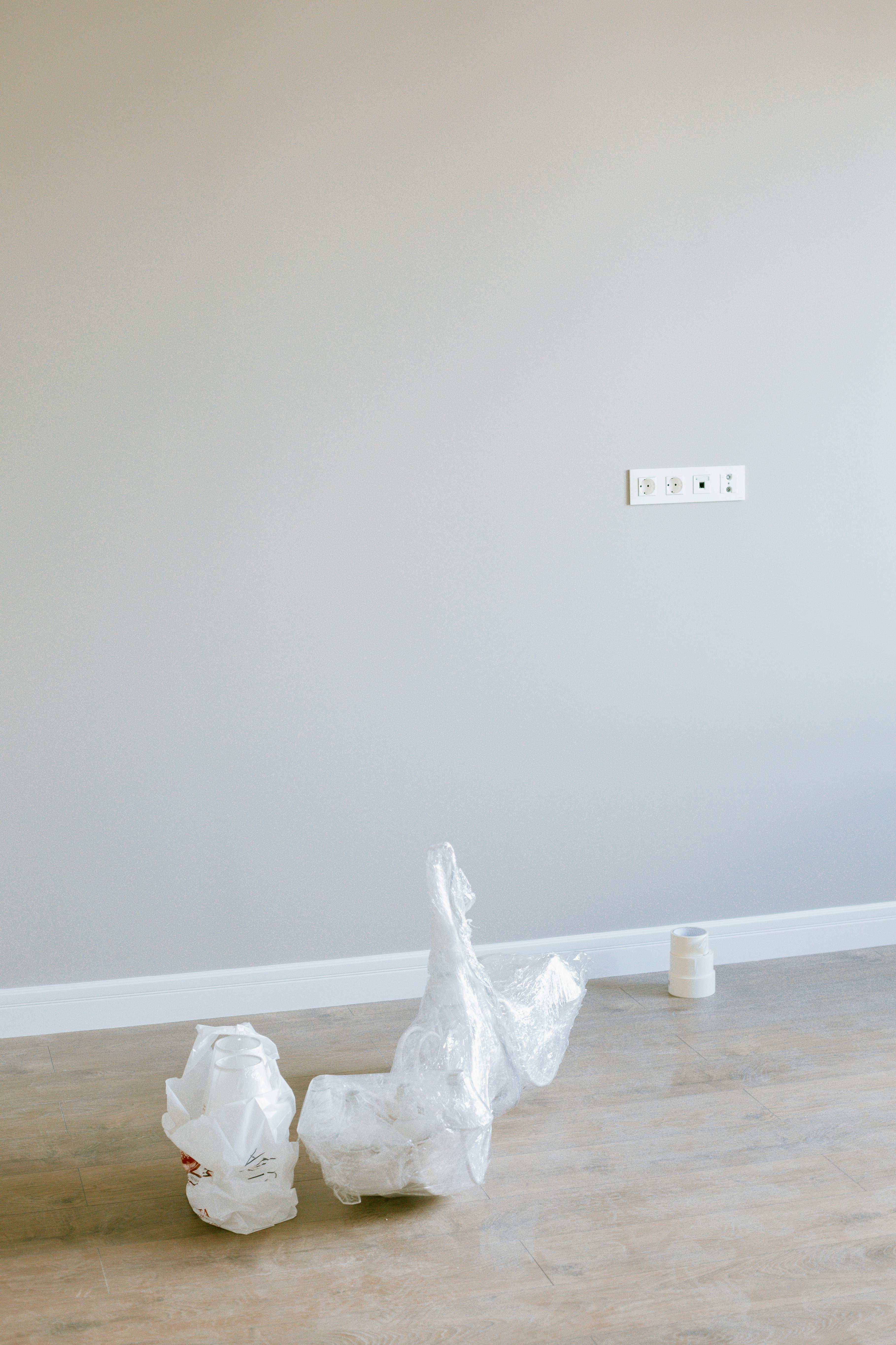 Minimalist room with wrapped objects on wooden floor and gray wall.