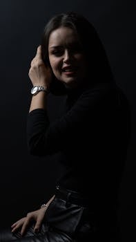 Portrait of a woman in darkness, highlighting her watch and stylish outfit.