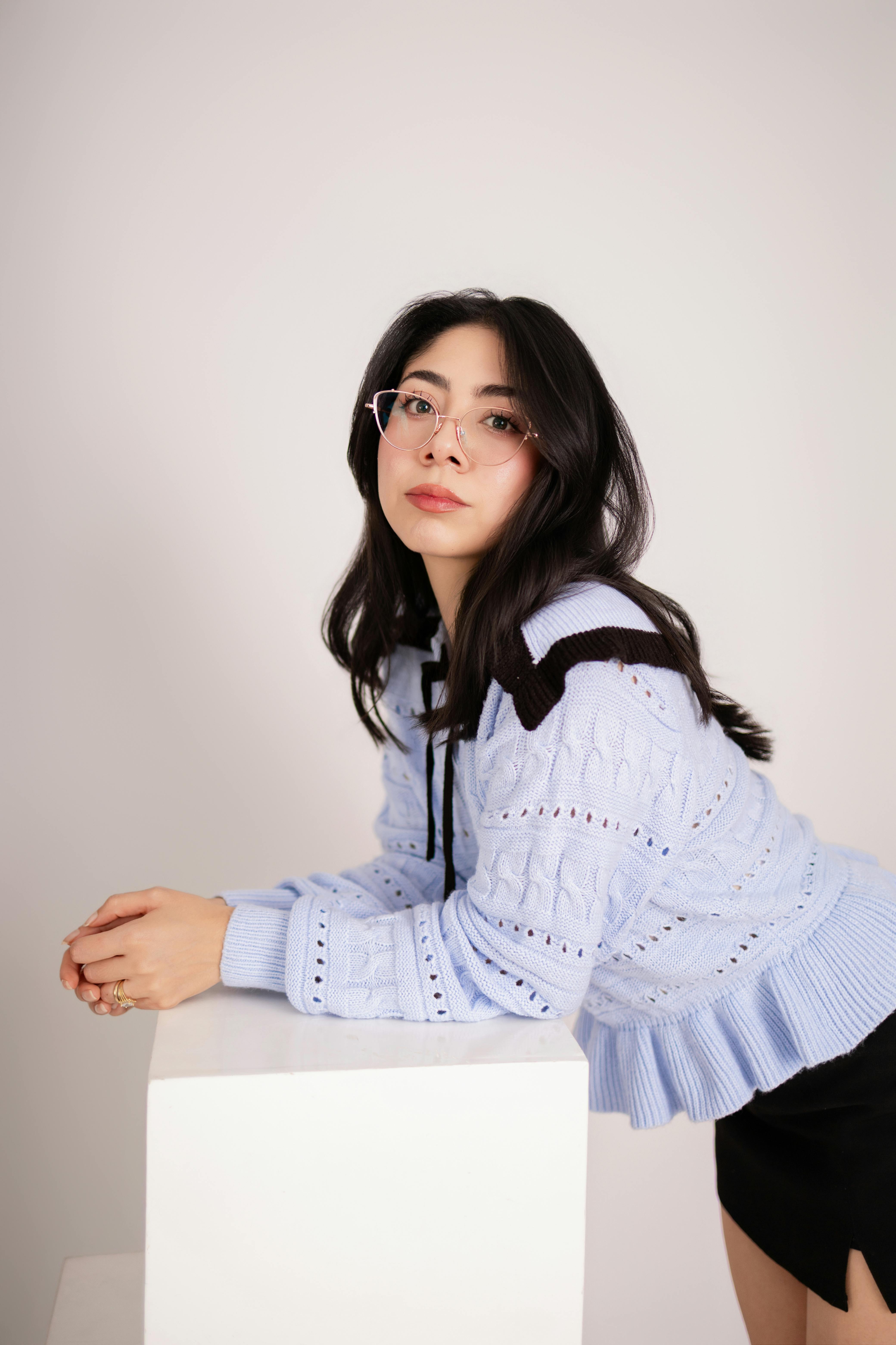 Gratis Elegante ritratto in interni di una giovane donna con gli occhiali appoggiata a un cubo bianco in un ambiente moderno e minimalista. Foto a disposizione