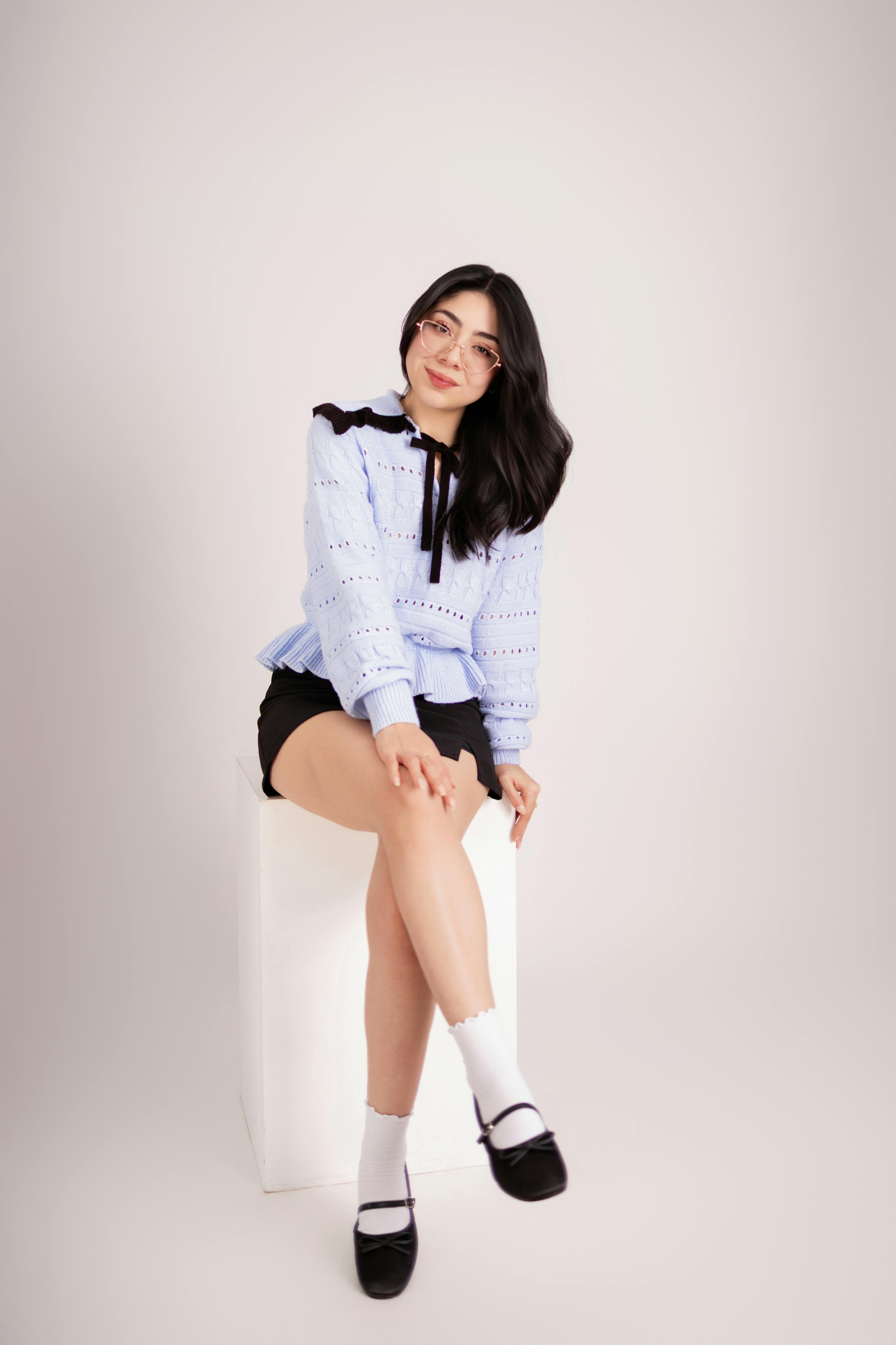Free Stylish young woman sitting on a white cube, showcasing modern fashion indoors. Stock Photo