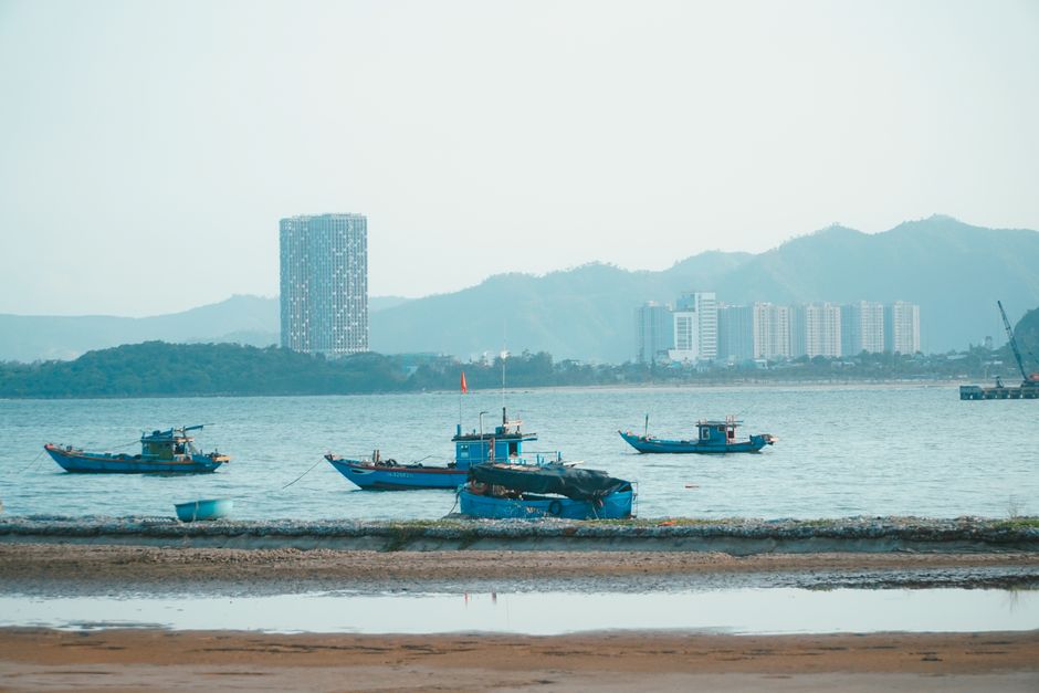Scenic view of fishing boats in Da Nang harbor with urban skyline and mountains.