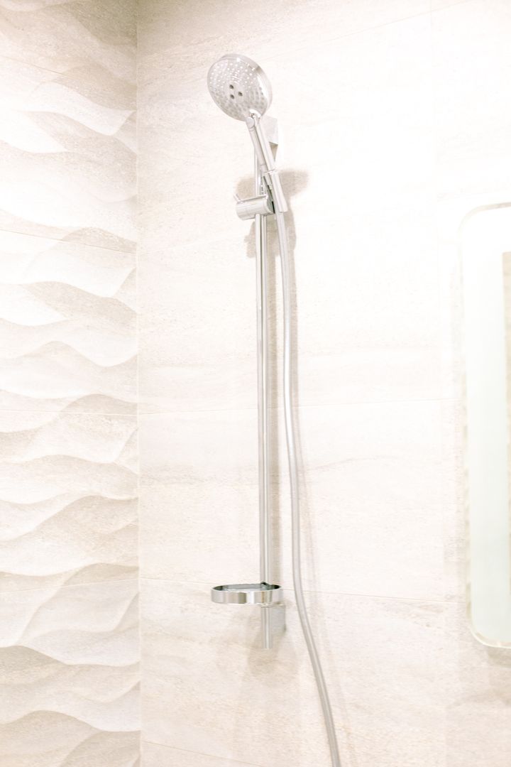 Chrome hand shower on its wall rail against pale wave-textured bathroom tiles