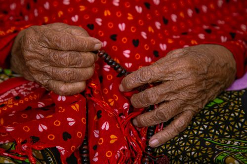 Free Close-up of elderly hands holding prayer beads on a vibrant fabric background. Stock Photo
