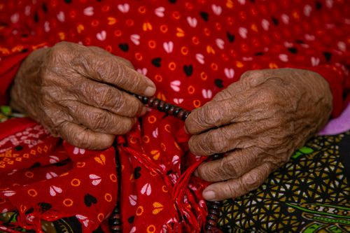 Free Close-up of an elderly person's hands holding prayer beads, draped in colorful patterned fabric. Stock Photo