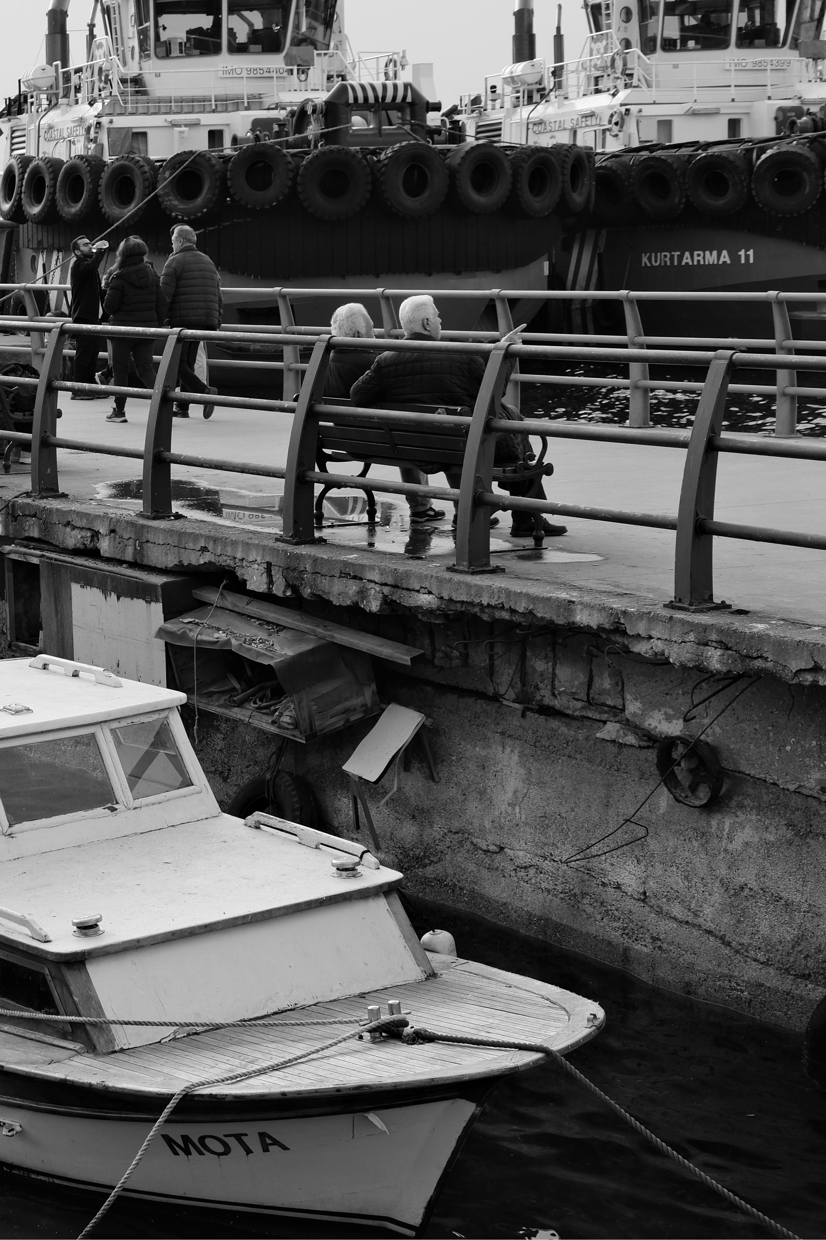 A peaceful black and white scene of people on a bench by the Istanbul harbor.