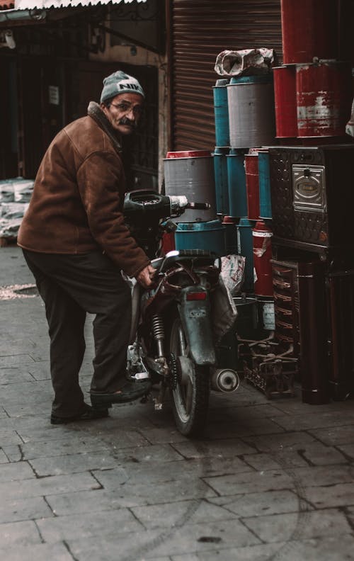 オートバイの横に立っている茶色のジャケットの男
