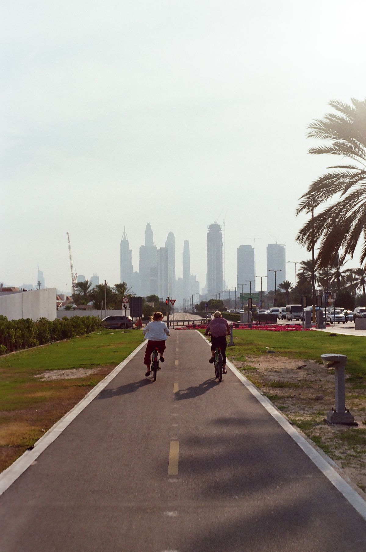 Two cyclists riding along a dedicated path toward the Dubai skyline at dusk