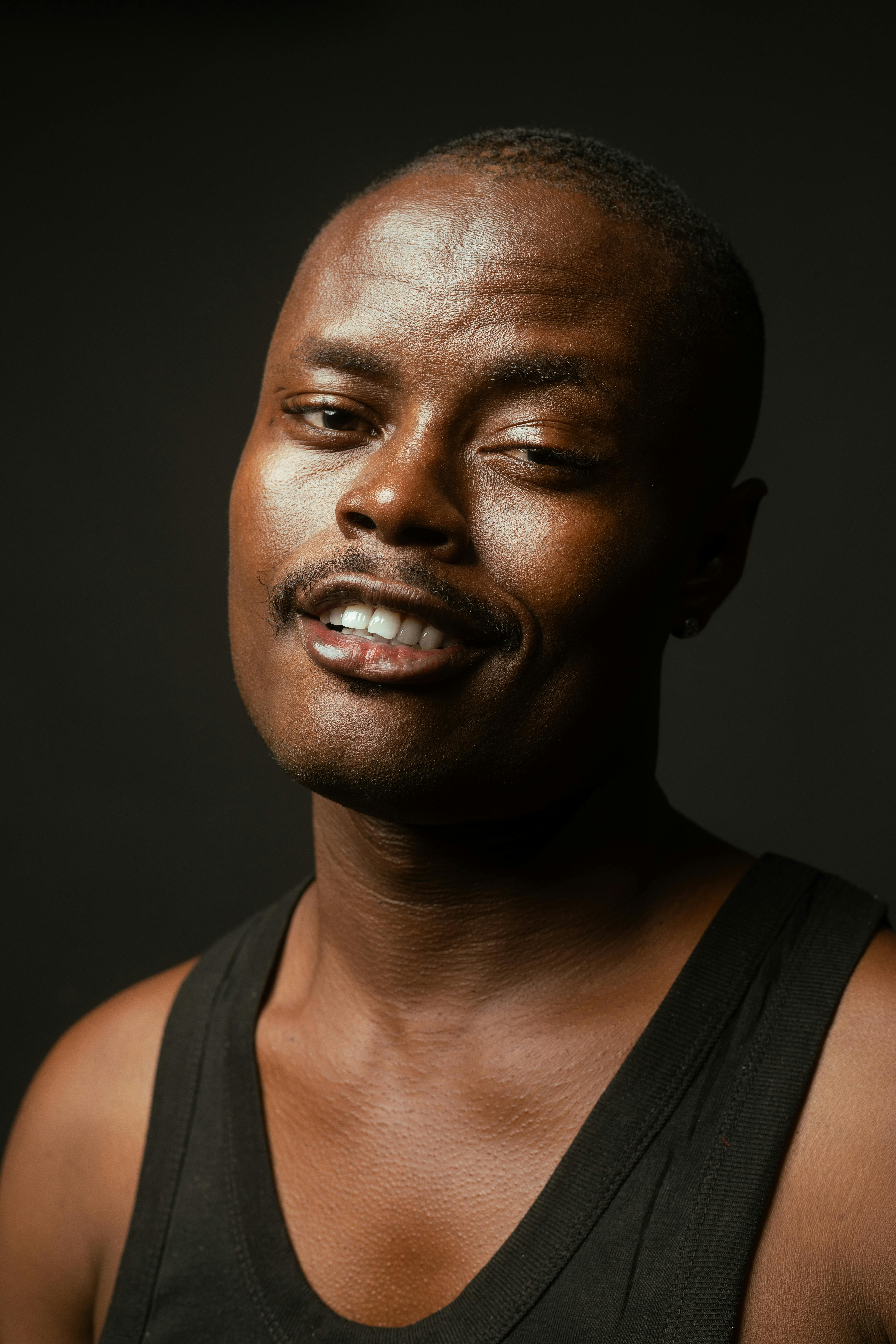 ฟรี ภาพถ่ายระยะใกล้ของชายหนุ่มยิ้มแย้มในเสื้อกล้ามสีดำ โดยมีฉากหลังเป็นสีเข้ม คลังภาพถ่าย