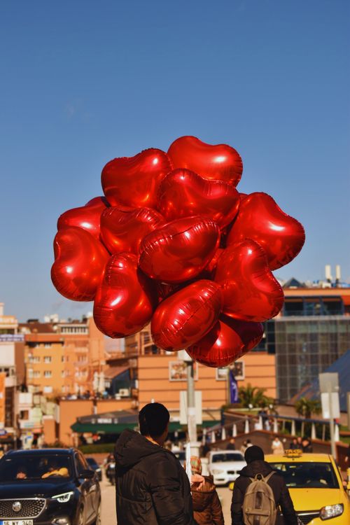 Free Bright red heart balloons float above a busy street in Türkiye, capturing attention and adding charm. Stock Photo