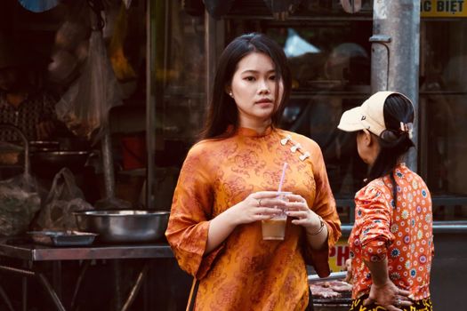 A young woman in an orange traditional dress holds a drink outdoors, adding cultural vibrancy.