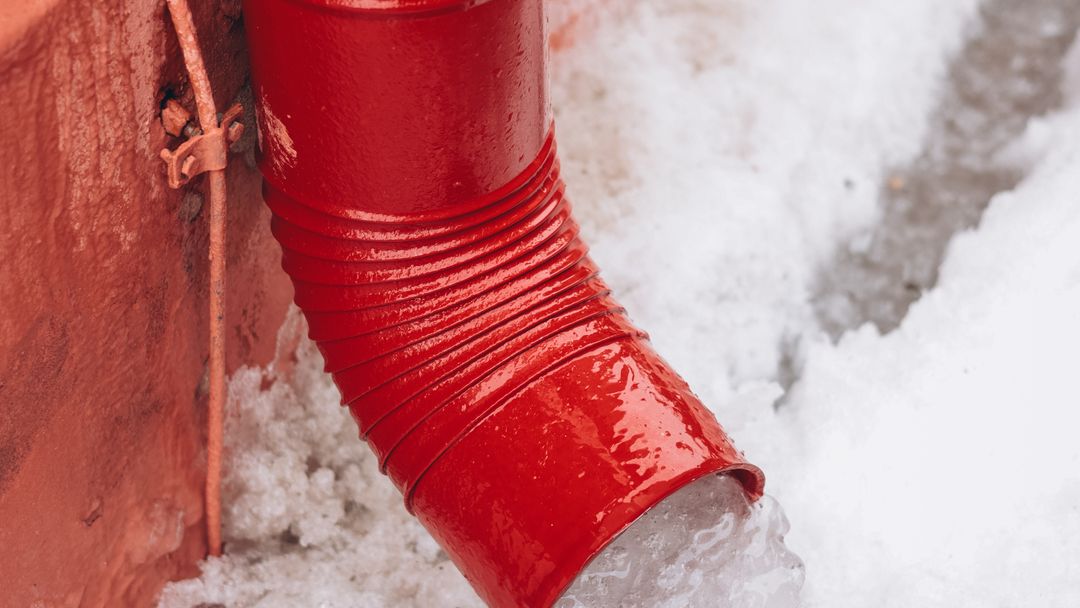 A drainpipe outside in winter with snow melting around it