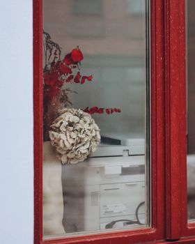 A peek into a cozy room with dried flowers through a red framed window, creating a warm ambiance.