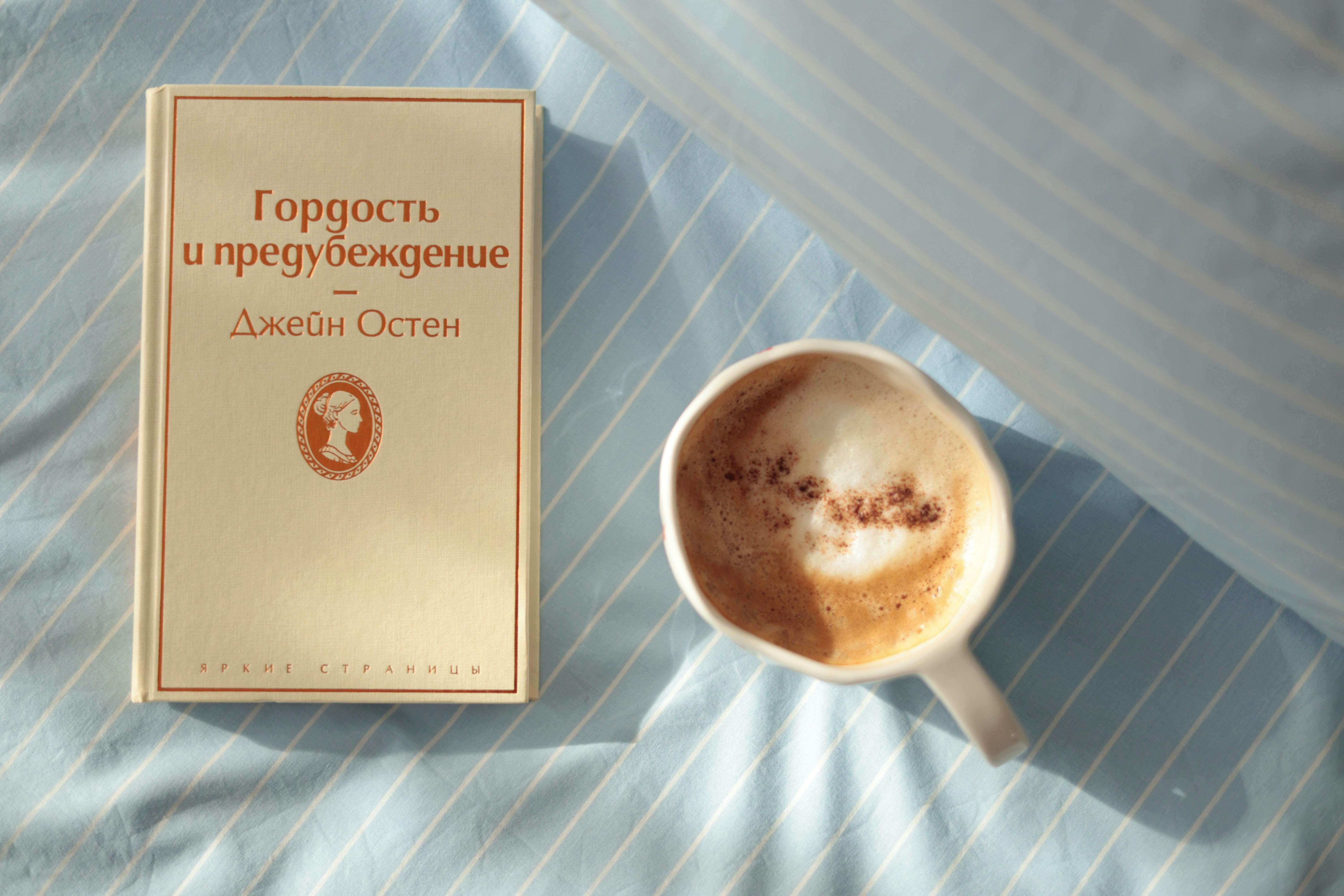 ฟรี ภาพบรรยากาศยามเช้าอันสงบเงียบ กับกาแฟหนึ่งถ้วยและหนังสือหนึ่งเล่ม บนผ้าปูที่นอนลายทาง คลังภาพถ่าย