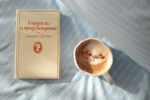 A calm morning scene with a cup of coffee and a book on a striped bedsheet.
