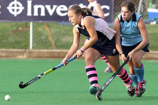Dynamic action shot of women playing field hockey during a competitive match on a grass field.