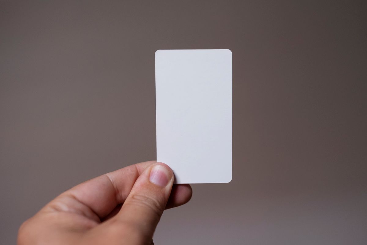 Close-up of a hand holding a blank white card with a neutral background