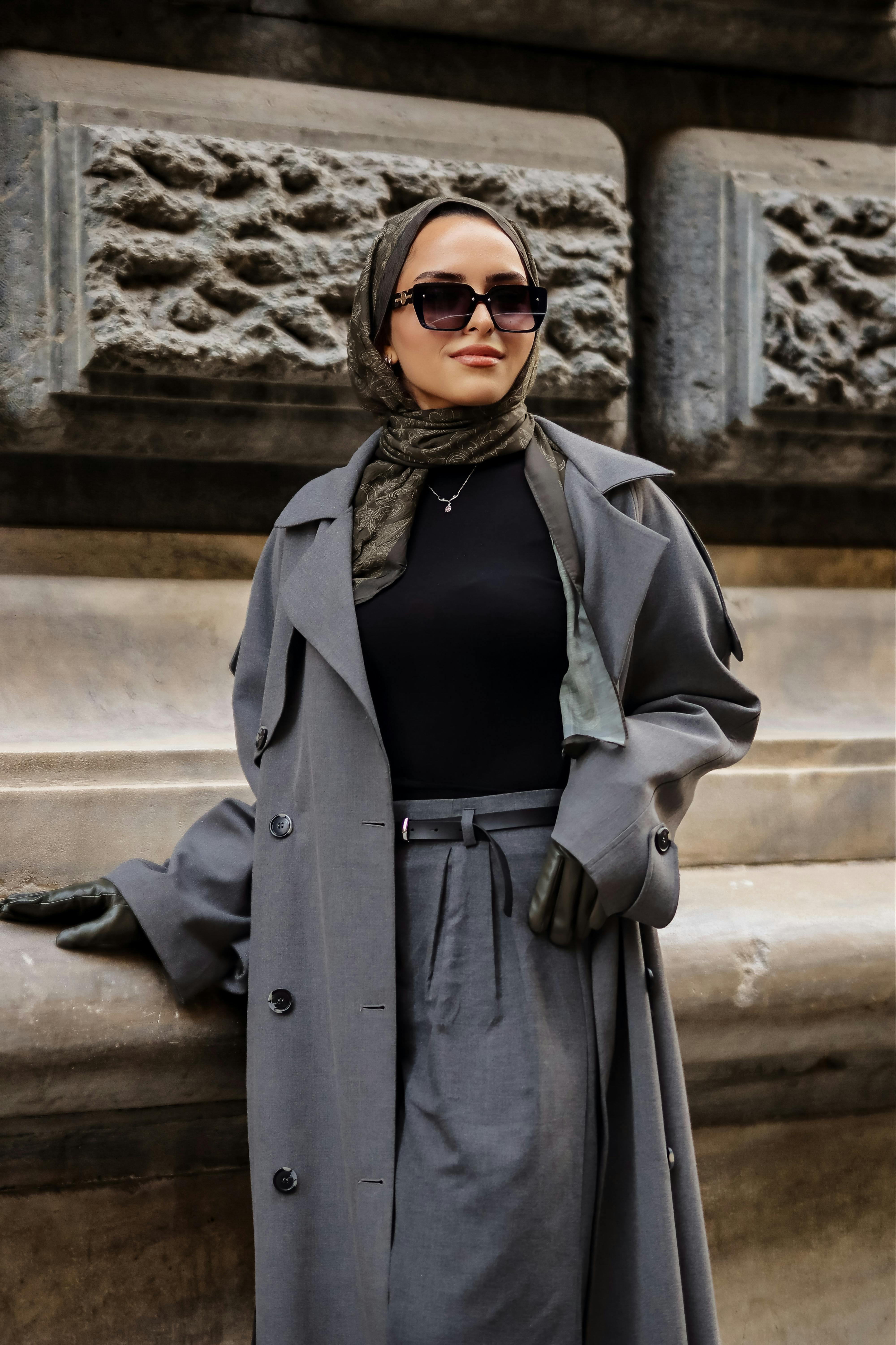 Gratis Una donna alla moda con un cappotto grigio e un foulard in testa posa all'aperto, esprimendo sicurezza e stile. Foto a disposizione