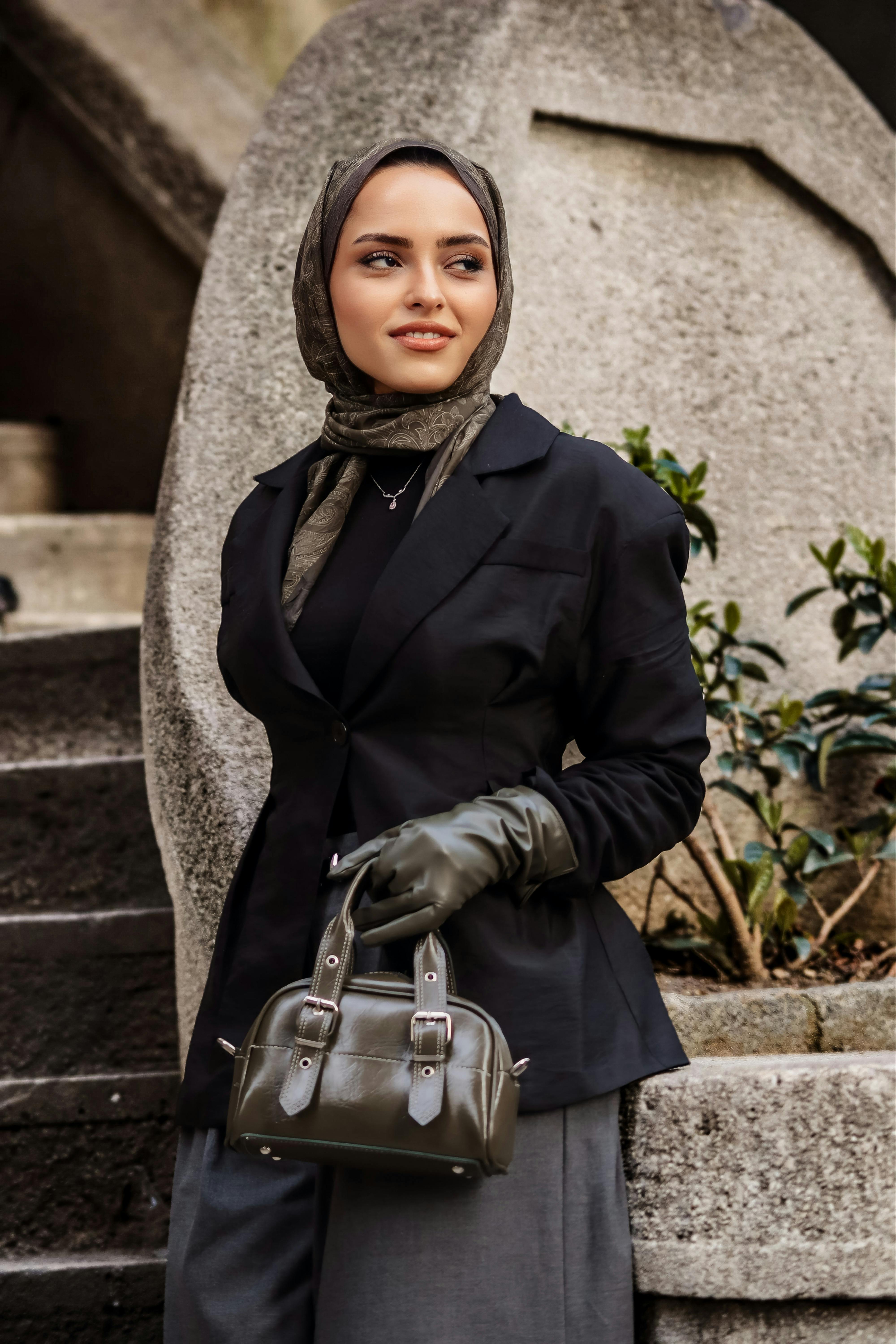 Gratis Una donna elegante con hijab e guanti di pelle posa all'aperto. Moda moderna in un contesto urbano. Foto a disposizione