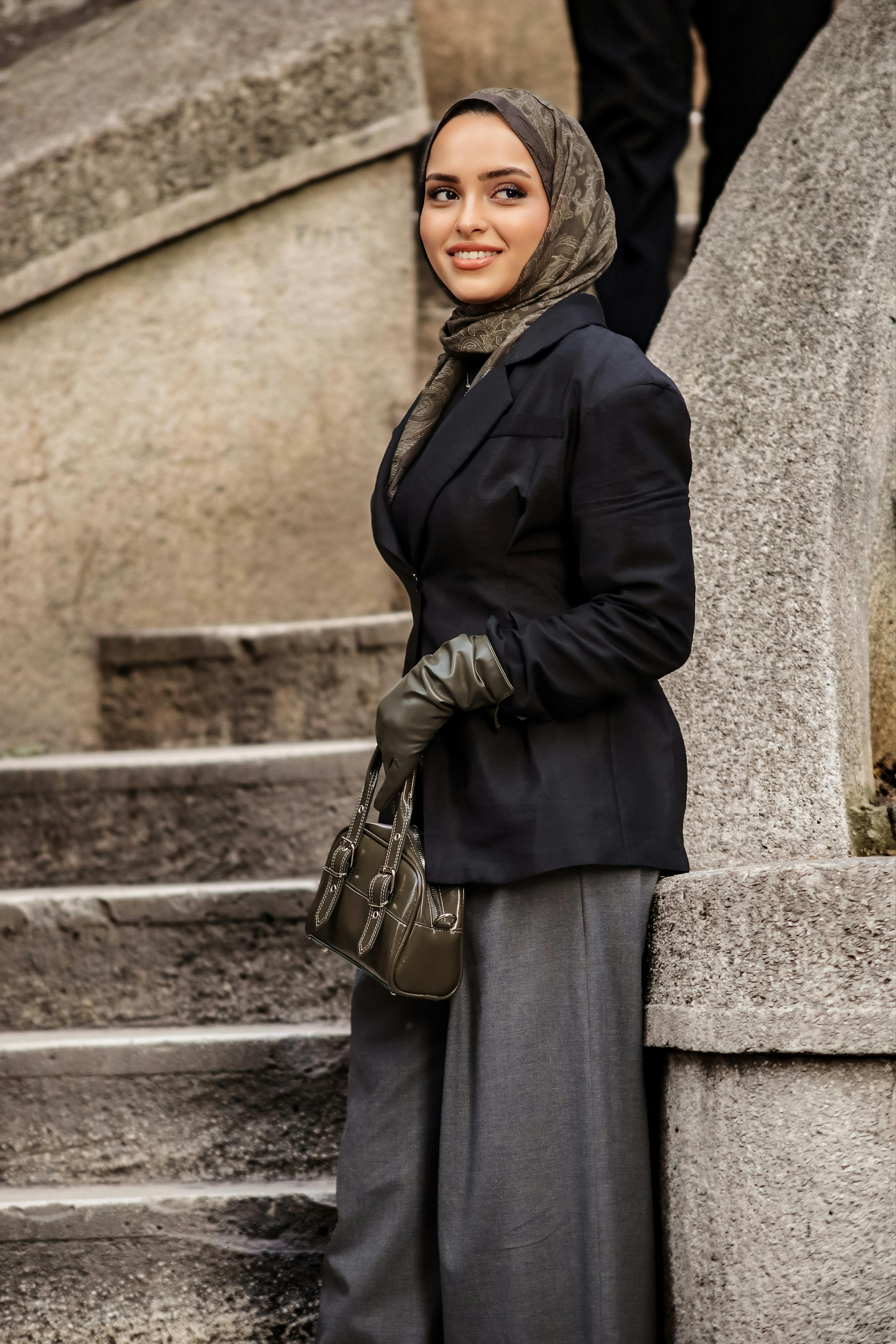 ฟรี หญิงสาวแต่งตัวมีสไตล์ สวมฮิญาบและถุงมือ ยืนอยู่บนบันไดหิน ดูสง่างาม คลังภาพถ่าย