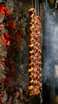 Deliciously grilled meat skewers cooking on an open flame, surrounded by smoky coals.