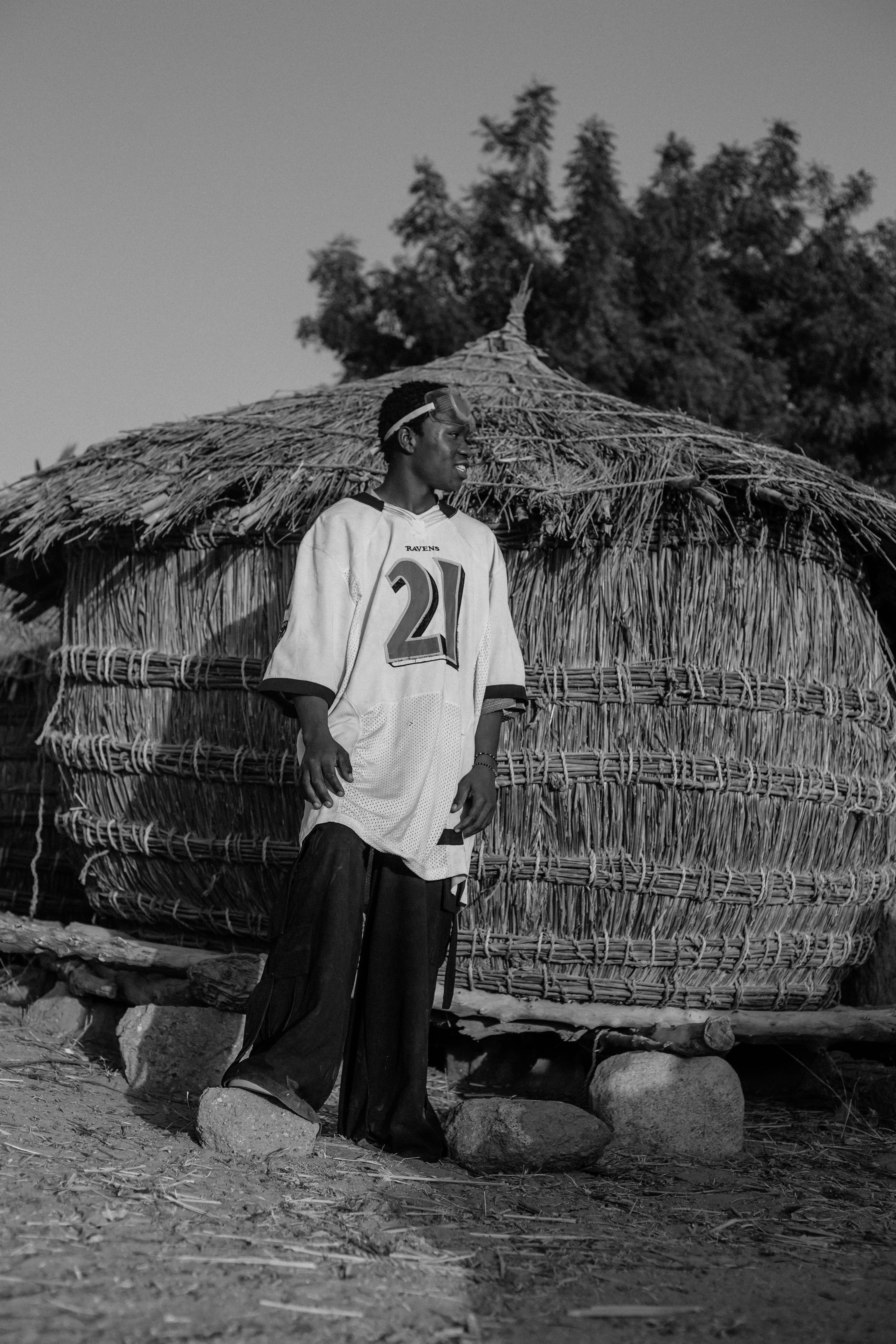Gratis Ritratto in bianco e nero di un giovane uomo vicino a una capanna di paglia in Nigeria. Foto a disposizione