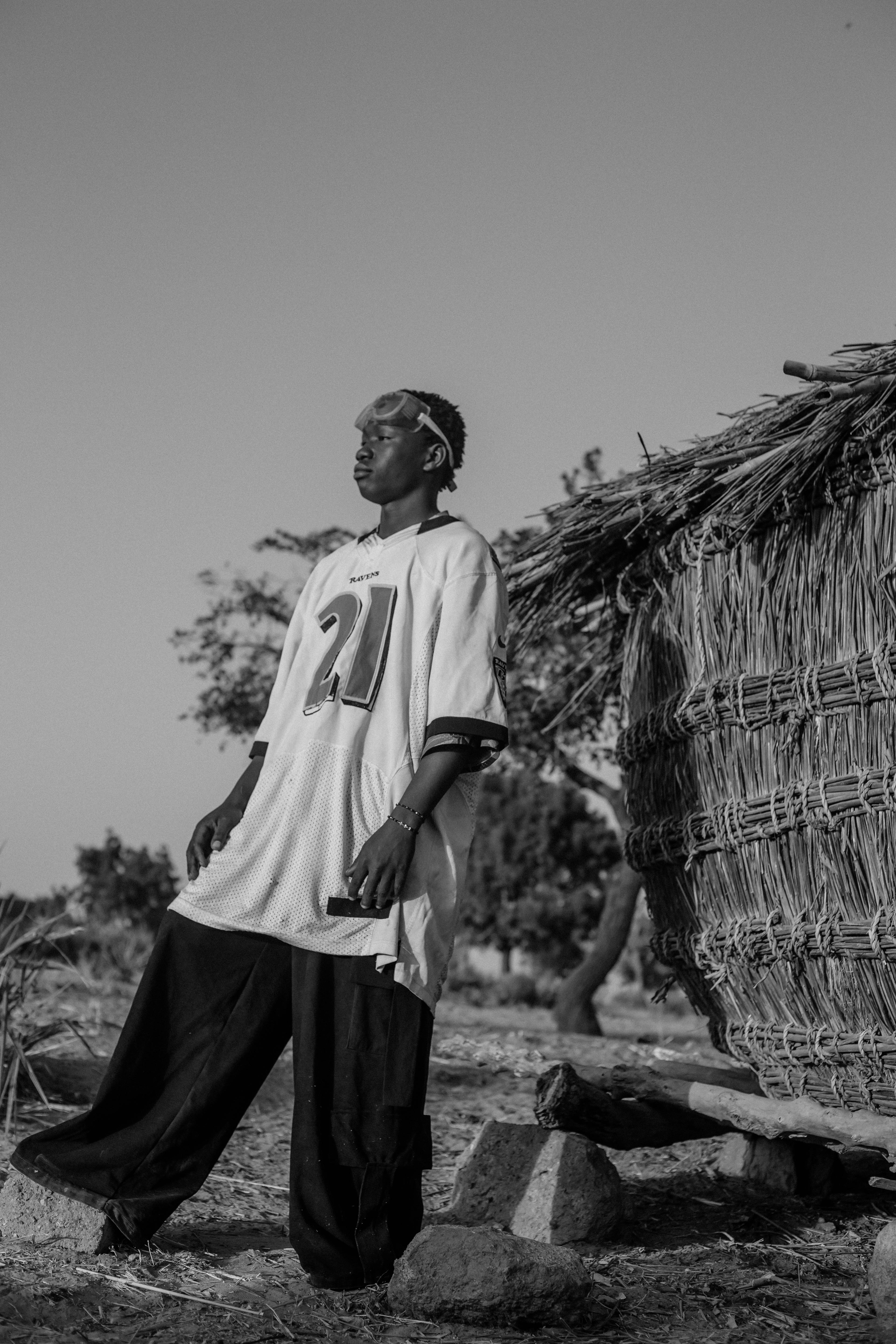 ฟรี ภาพถ่ายขาวดำที่โดดเด่นของชาวนาชาวไนจีเรียคนหนึ่งยืนอยู่กลางแจ้งใกล้กระท่อมแบบดั้งเดิม คลังภาพถ่าย