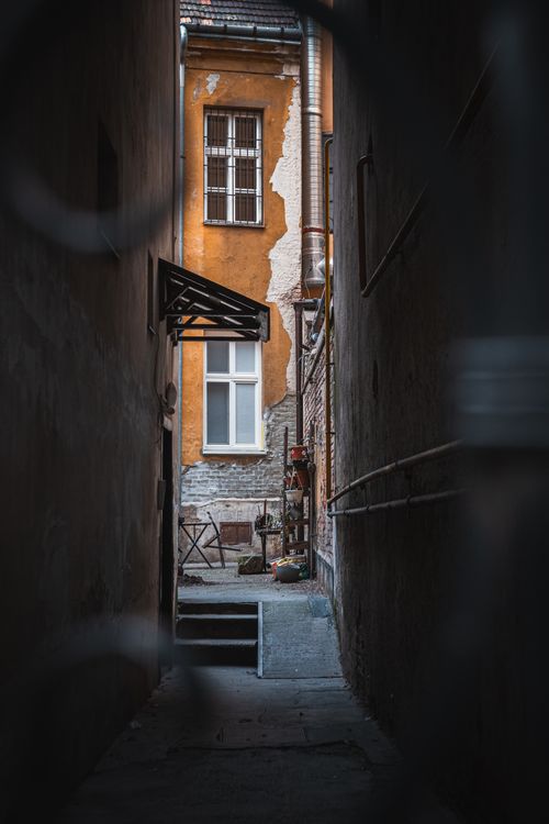Free A narrow urban alleyway opening into a rustic courtyard with an orange-stucco building facade. Stock Photo