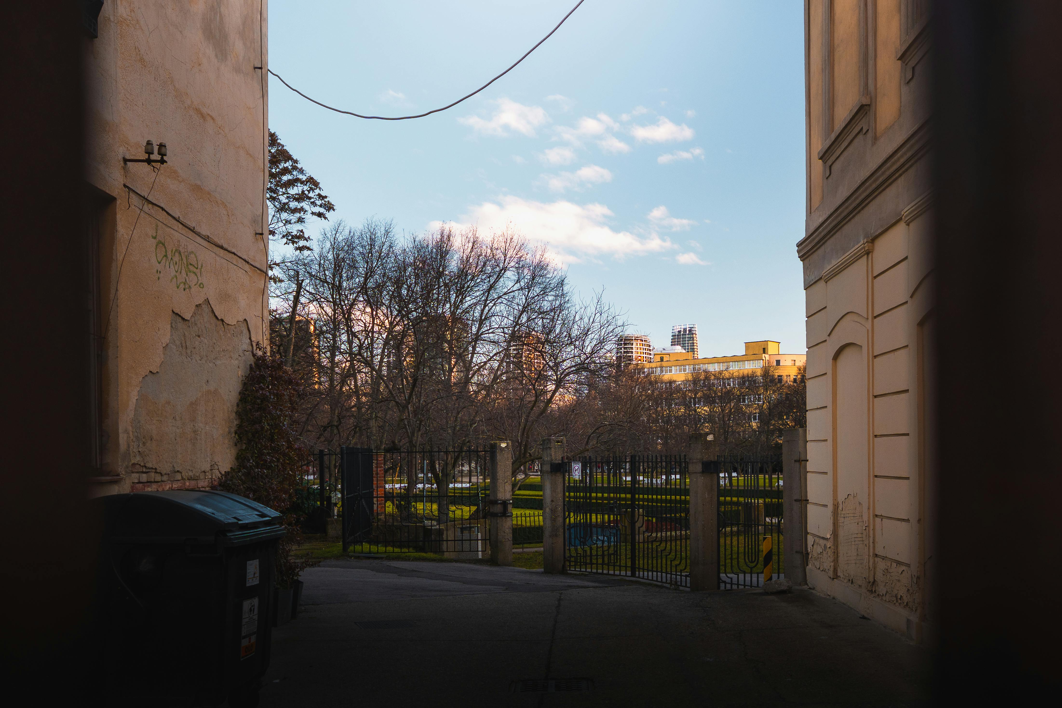 Gratis Uno stretto vicolo che conduce a edifici illuminati dal sole e ad alberi spogli in inverno, incorniciati da antiche architetture urbane. Foto a disposizione