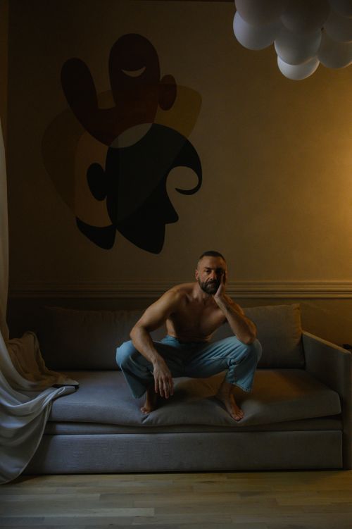 Free Bearded man sitting on a sofa, lost in thought, under moody lighting in an art-decorated room. Stock Photo