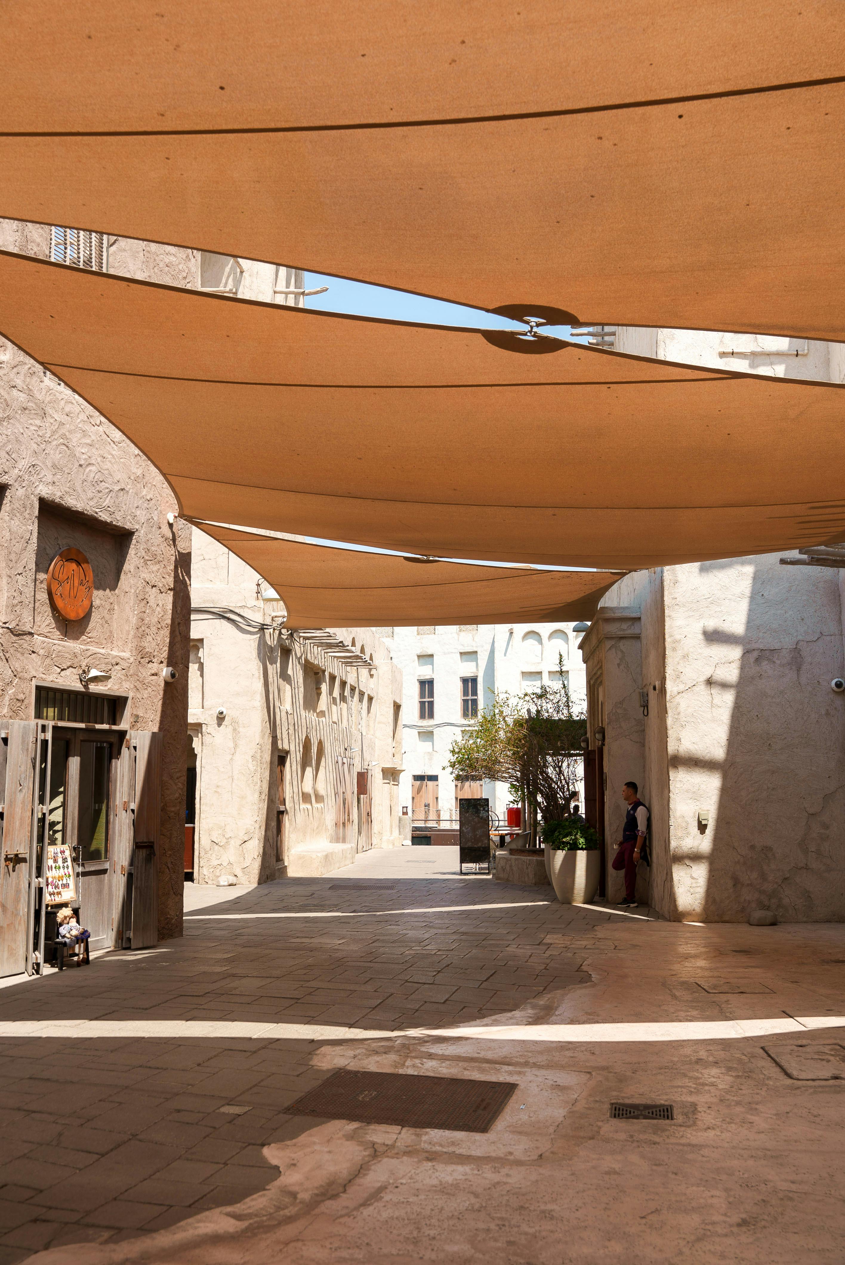 Gratis Naturskøn solbeskinnet gade i Dubai med skyggefulde lærredsoverdækninger, historisk arkitektur og rolig atmosfære. Lagerfoto