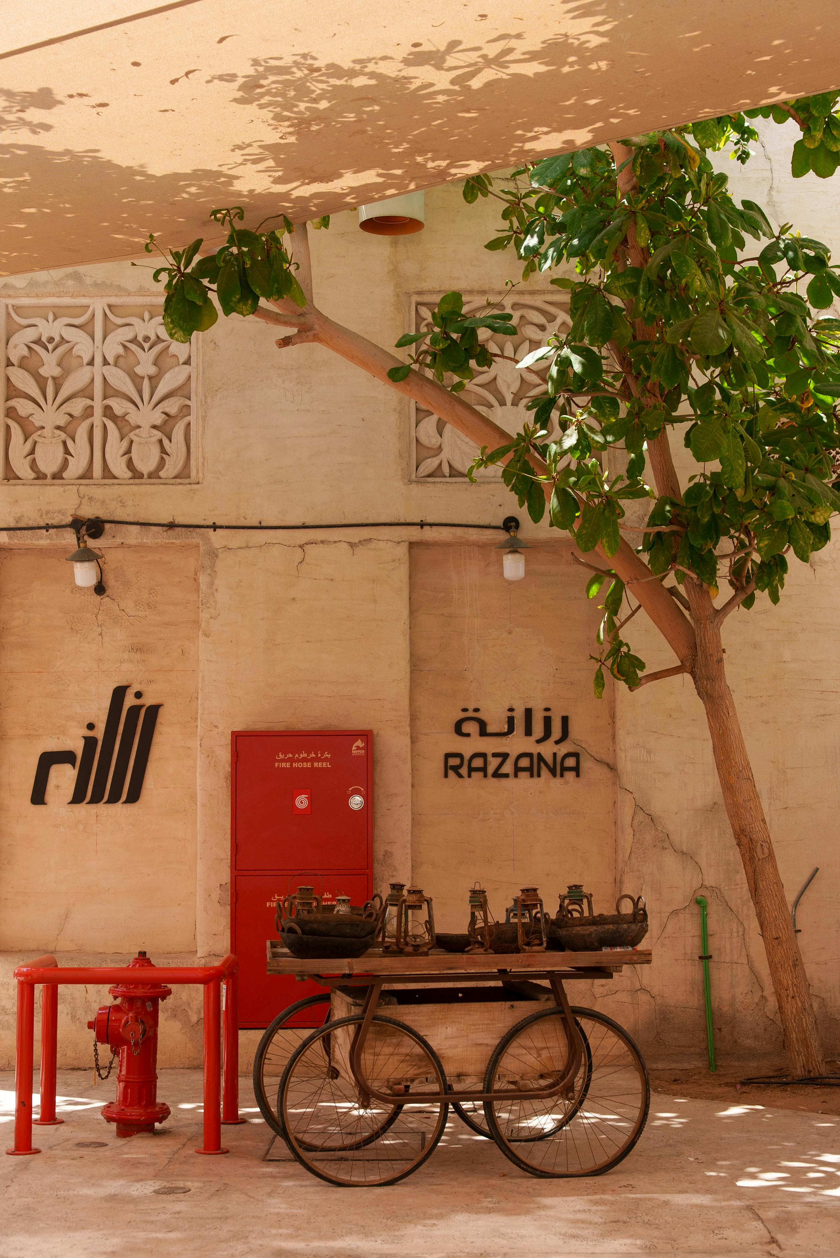 Ilmainen Viehättävä Dubain katukulma, jossa on vintage-kärryjä, arabialaisia ​​kylttejä ja rehevää vehreää kasvillisuutta. Kuvapankkikuva