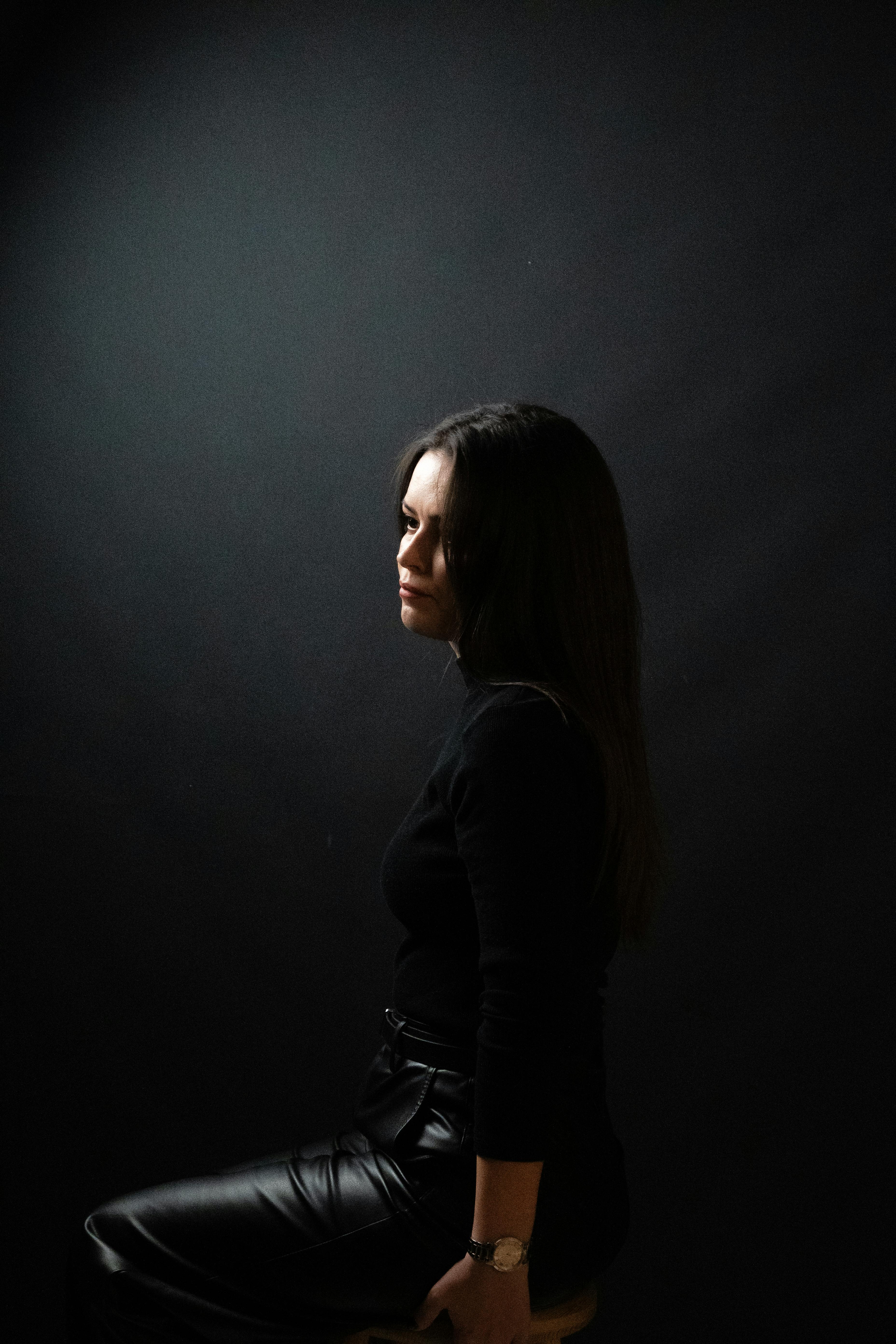 Gratis Profilo laterale malinconico di una donna seduta in una luce scura e drammatica. Foto a disposizione