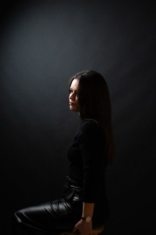 Free Moody side profile of a woman sitting in dark, dramatic lighting. Stock Photo