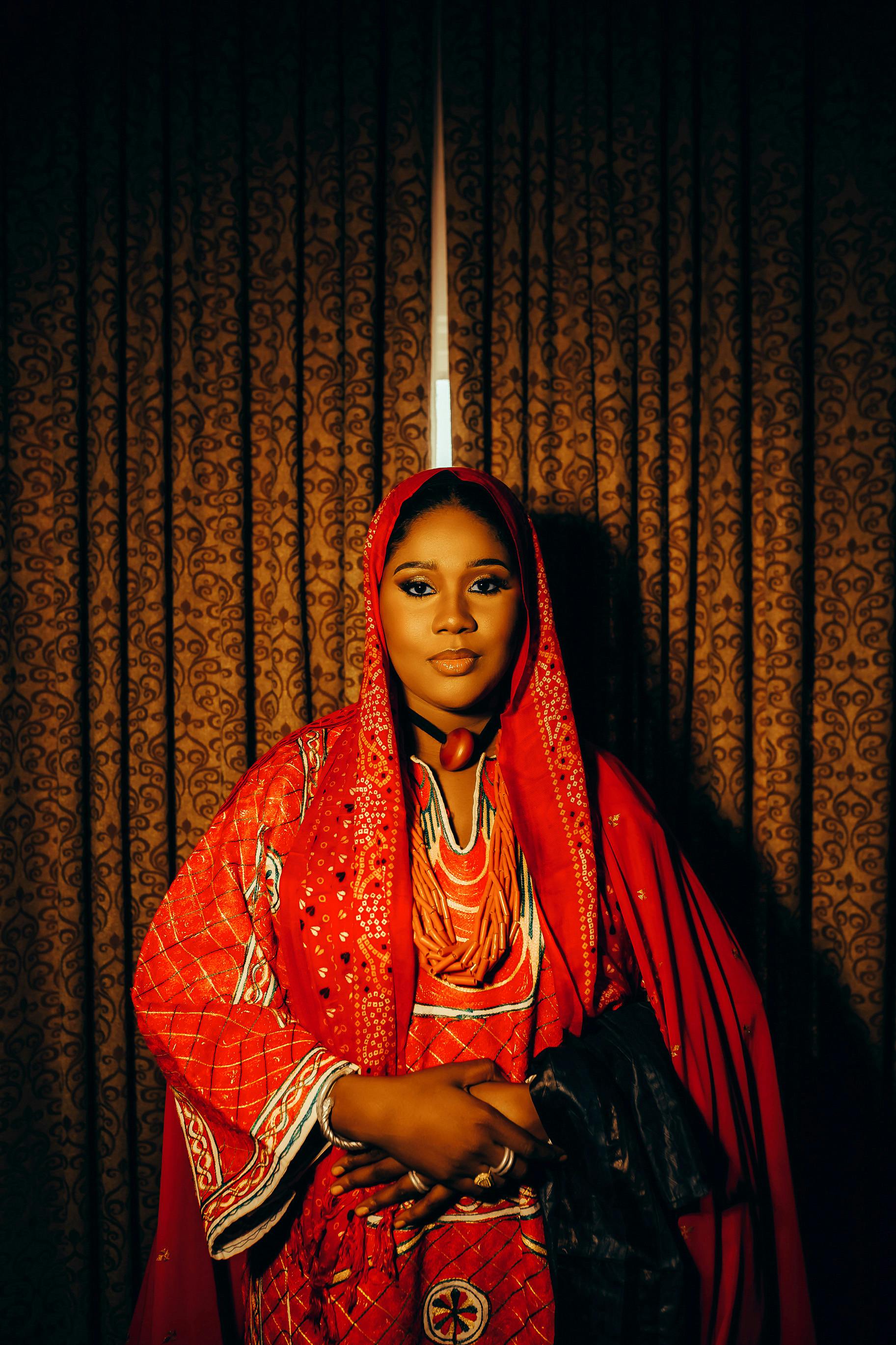 A woman in vibrant red traditional clothing stands gracefully indoors, conveying elegance and cultural richness.