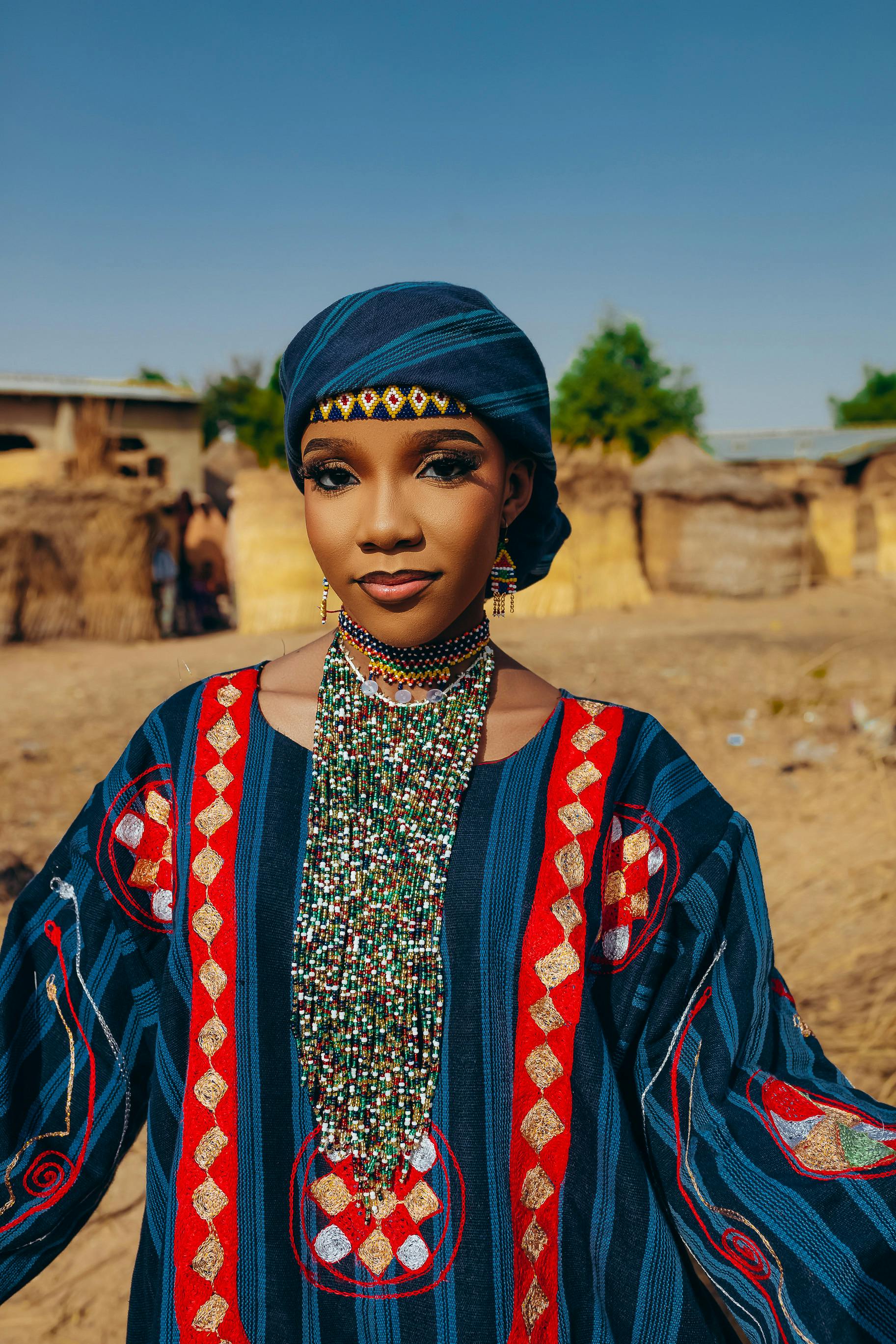 Portrait of a young woman in vibrant traditional African clothing outdoors.