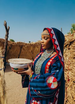 A woman in vibrant traditional African clothing holds a bowl outdoors, exuding cultural richness.