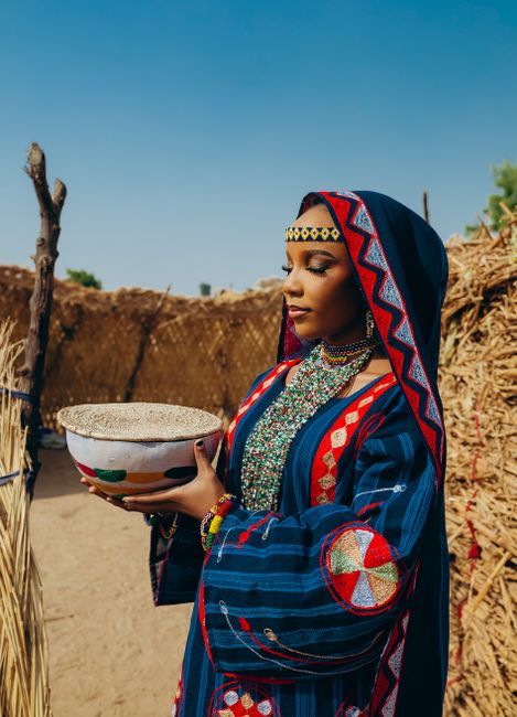 A woman in vibrant traditional African clothing holds a bowl outdoors, exuding cultural richness.