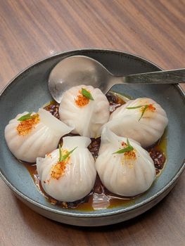 Freshly steamed dumplings served in a tangy chili sauce on a ceramic dish.