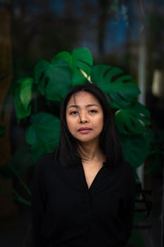 Elegant portrait of a woman standing against lush green monstera leaves, conveying a serene and natural vibe.