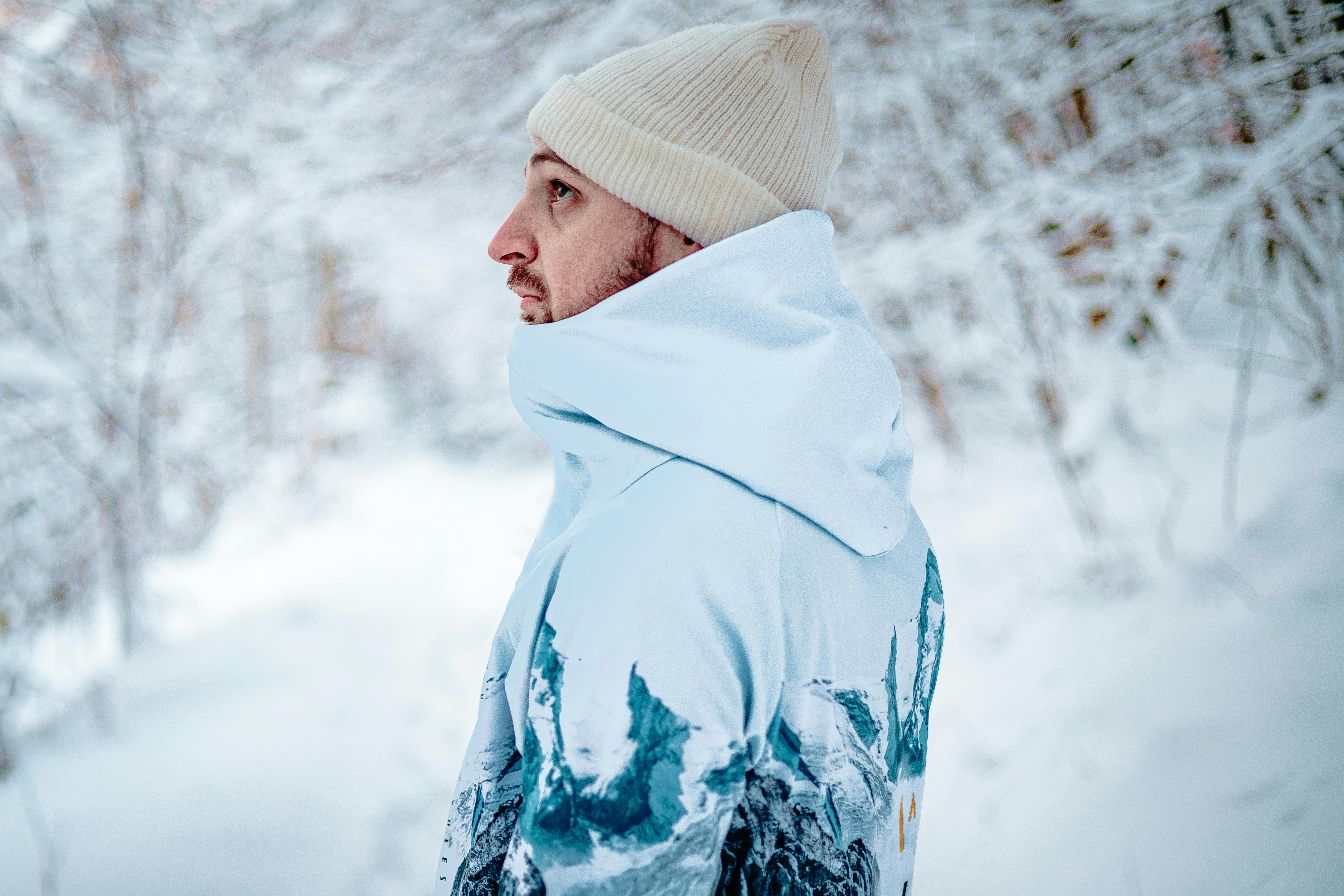 ฟรี ภาพถ่ายชายคนหนึ่งสวมเสื้อผ้ากันหนาวและหมวกไหมพรม ยืนอยู่ในป่าที่ปกคลุมไปด้วยหิมะ คลังภาพถ่าย