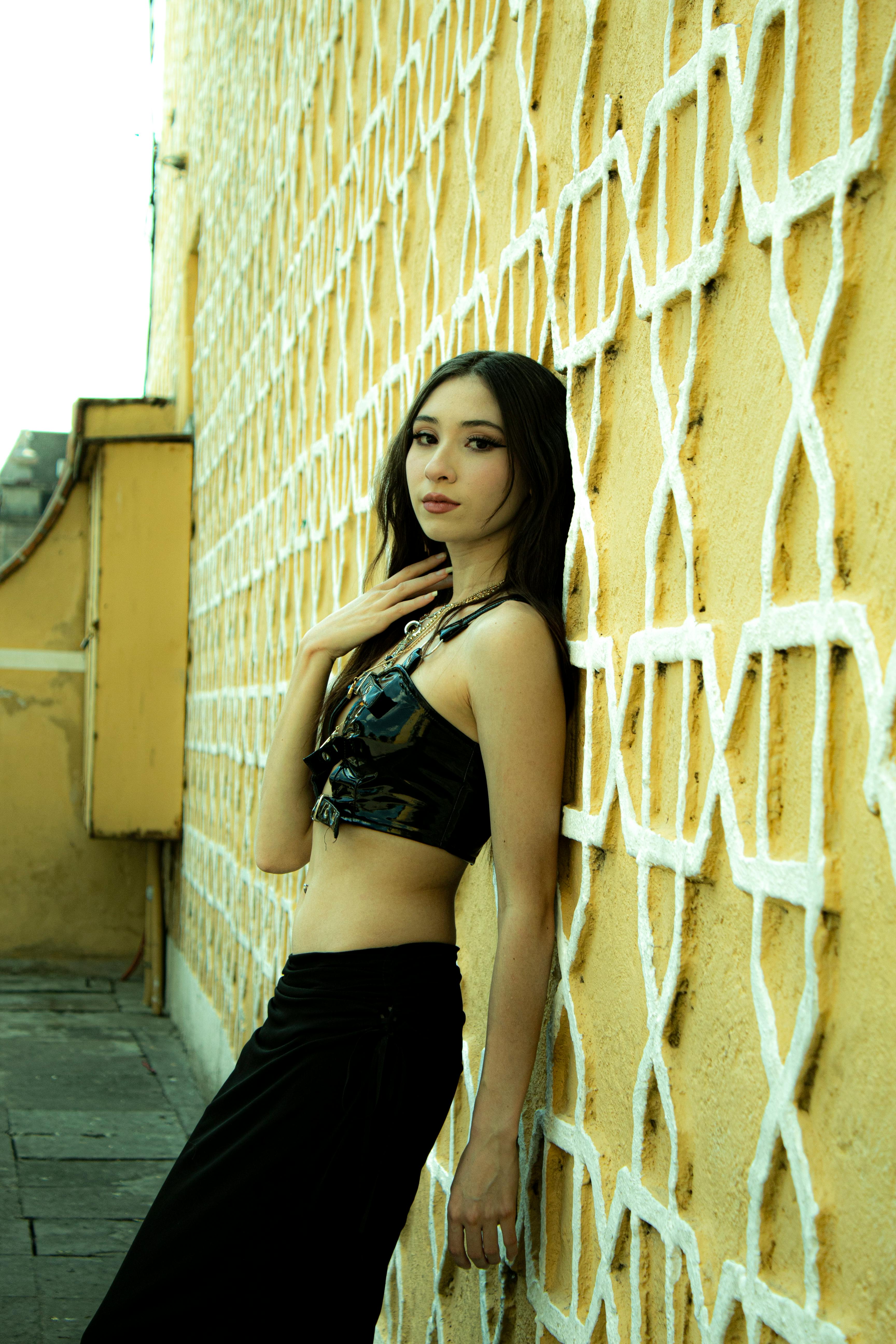 Gratis Una donna elegante in abito nero posa contro un muro giallo geometrico all'aperto. Foto a disposizione