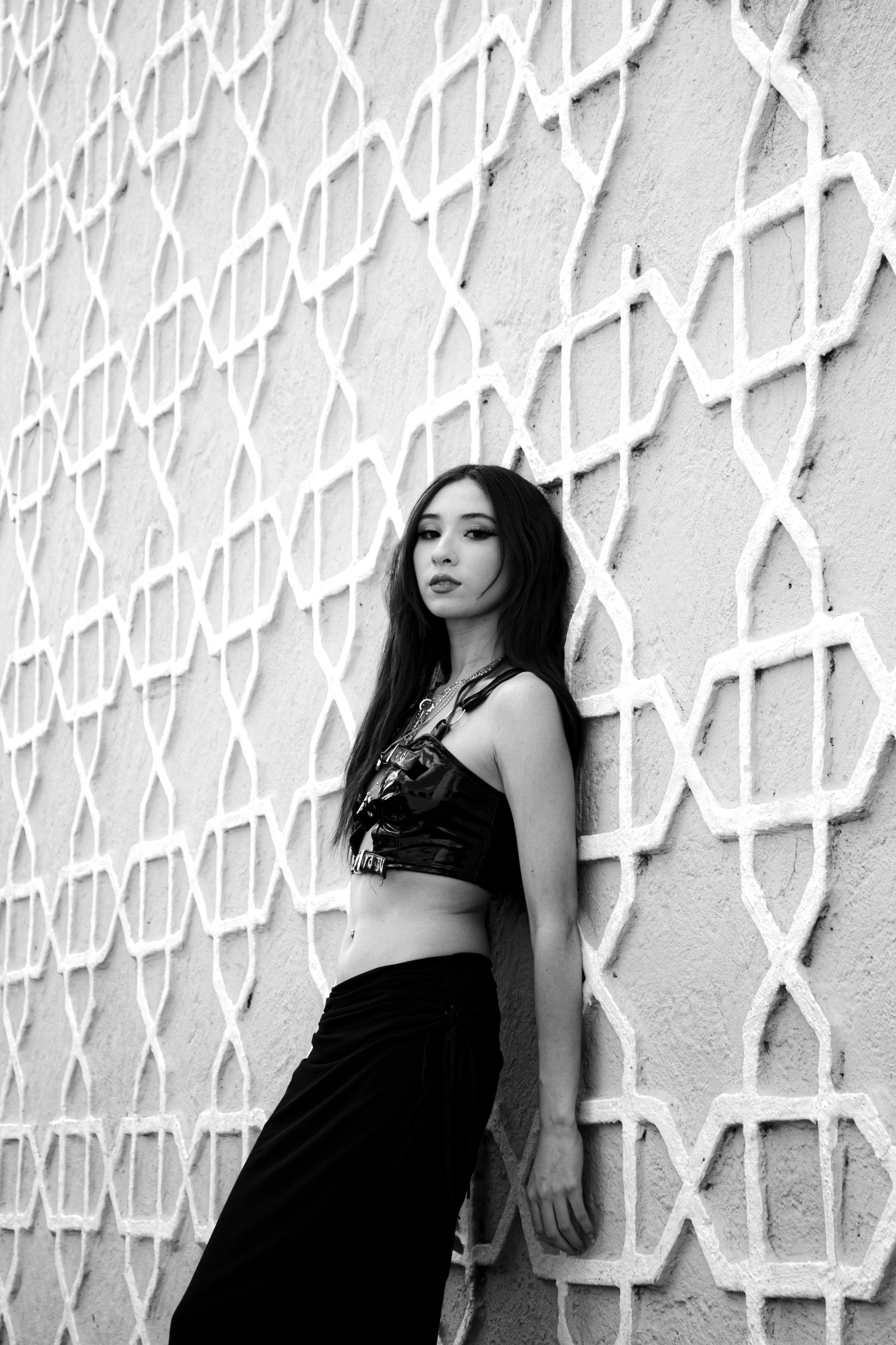 ฟรี ภาพถ่ายขาวดำสุดเก๋ของหญิงสาวคนหนึ่งยืนอยู่หน้ากำแพงที่มีลวดลายเรขาคณิต คลังภาพถ่าย